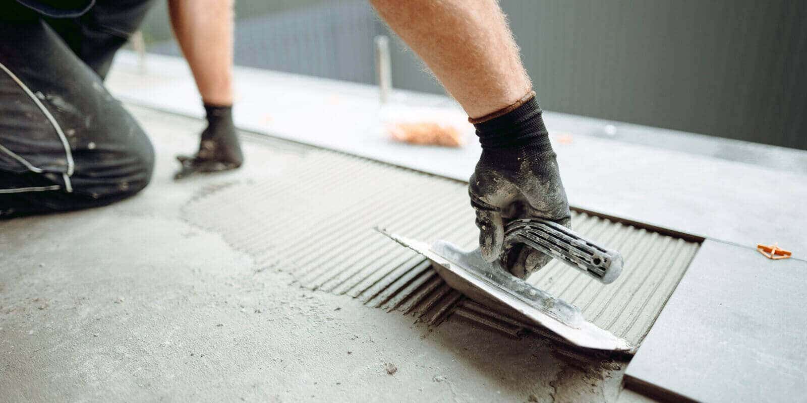 hand of professional tiler placing floor tiles on adhesive surface on balcony