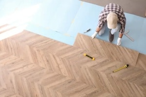 worker installing laminated wooden floor indoors